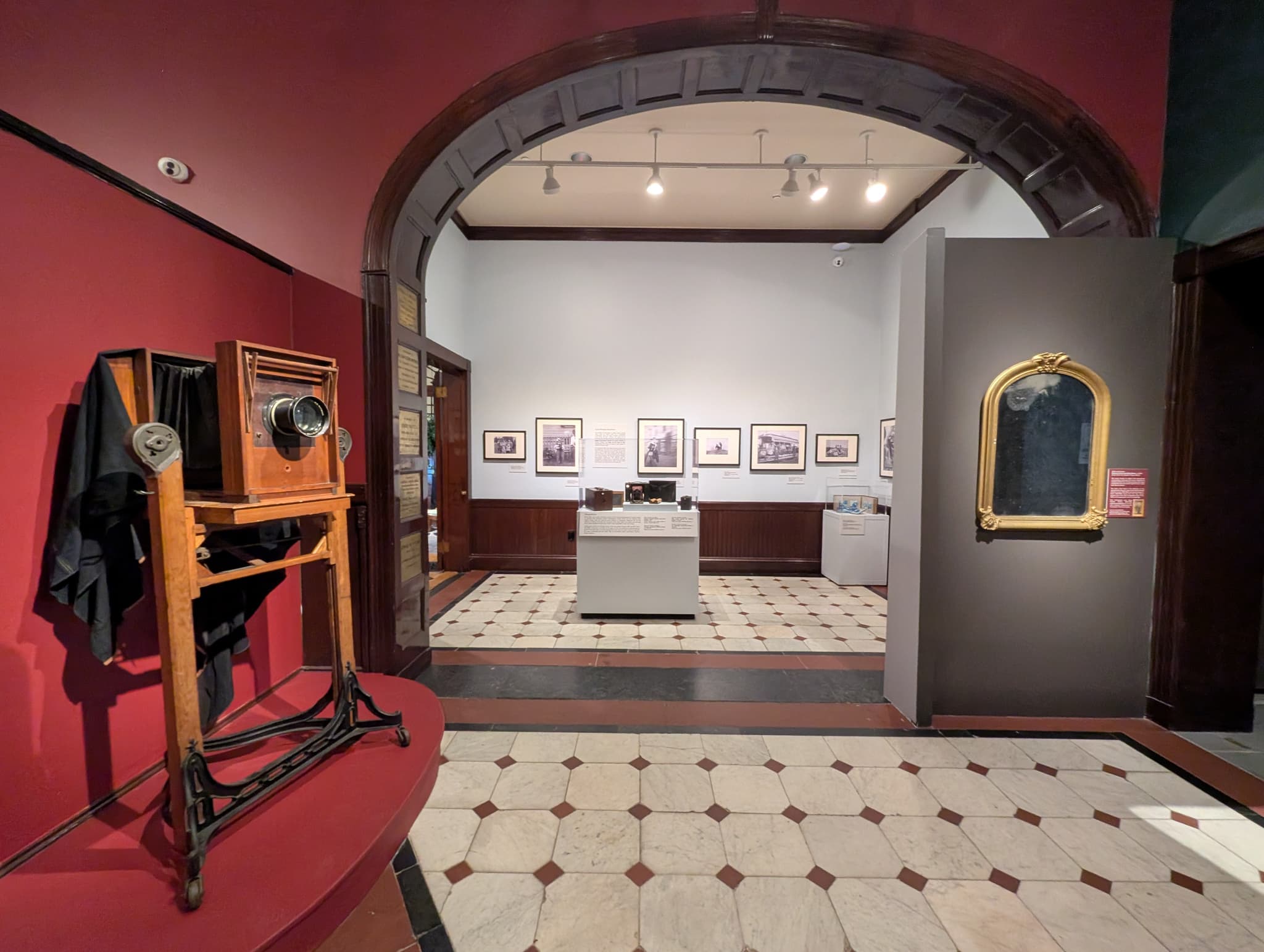 An installation view shows hanging portraits and a stereoscope.