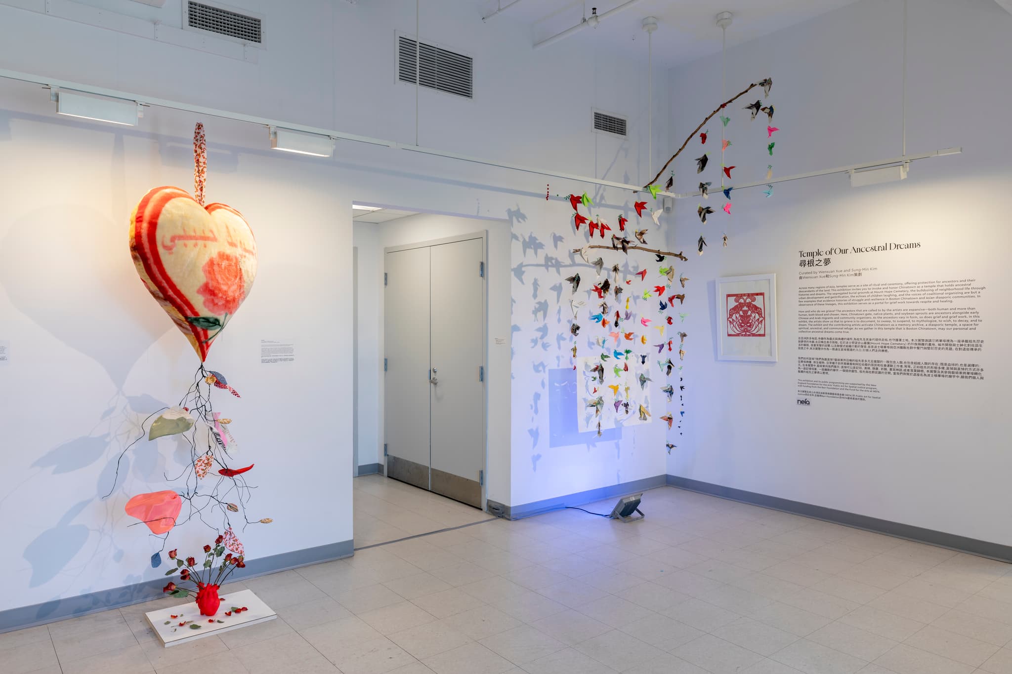 An installation view depicts a hanging heart sculpture and paper birds.