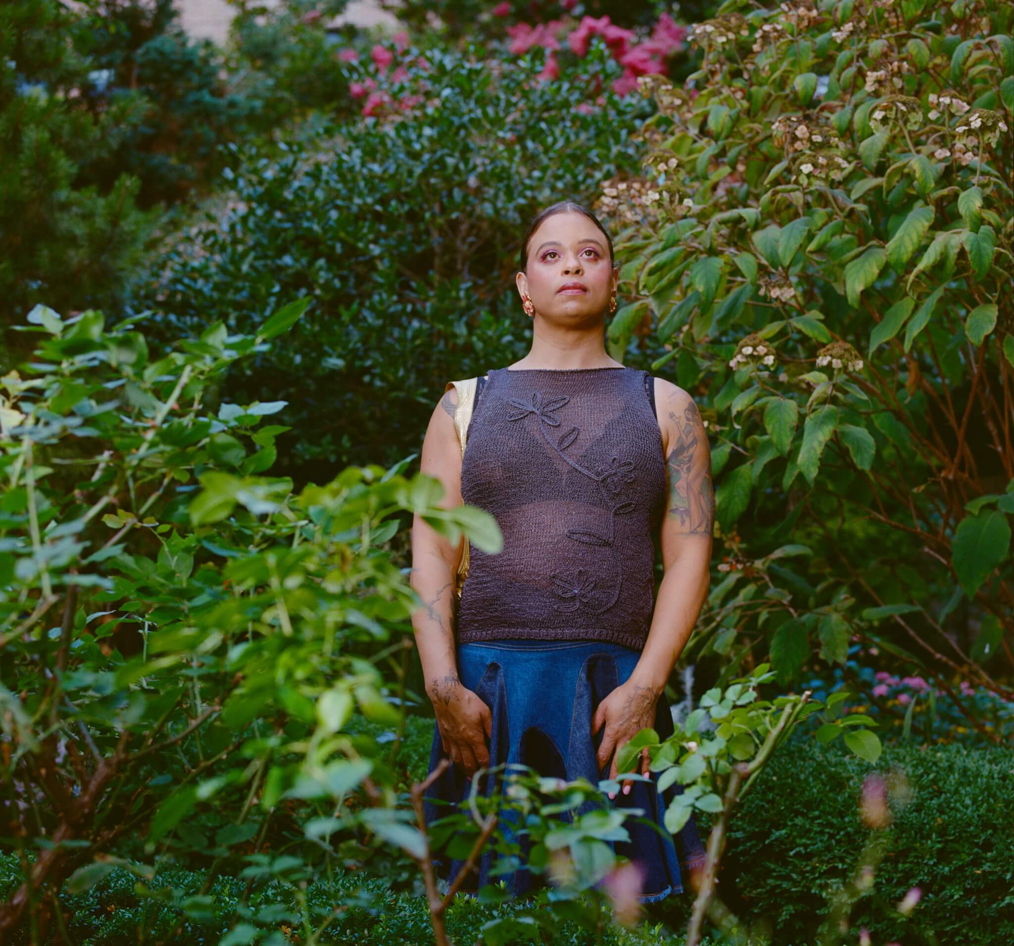 An individual stands among green bushes and trees in a garden.